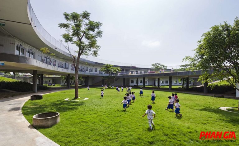 Trẻ em chạy trên sân cỏ, bao quanh dãy lớp hai tầng uốn cong, thiết kế mở, tại Đồng Nai.