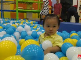 Bé gái mặc áo vàng ngồi giữa bể bóng xanh, trắng, vàng trong khu vui chơi do Phan Gia thực hiện
