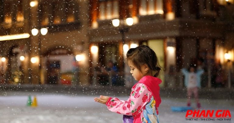 Bé gái mặc áo hồng ngắm và hứng tuyết nhân tạo trong khu vui chơi trong nhà