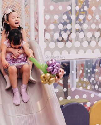 Lòng biết ơn là gì, Ý nghĩa và cách ứng dụng lòng biết ơn trong cuộc sống Hai bé gái ôm nhau trượt cầu trượt trong khu vui chơi, một bé cầm bó bong bóng hoa