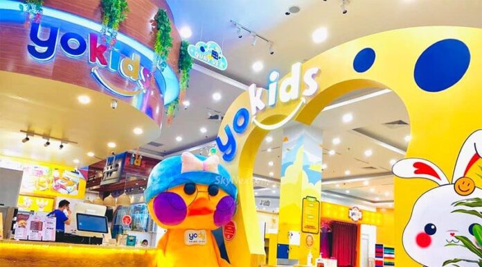 Cổng vào khu vui chơi trẻ em màu vàng với mascot gấu bông lớn